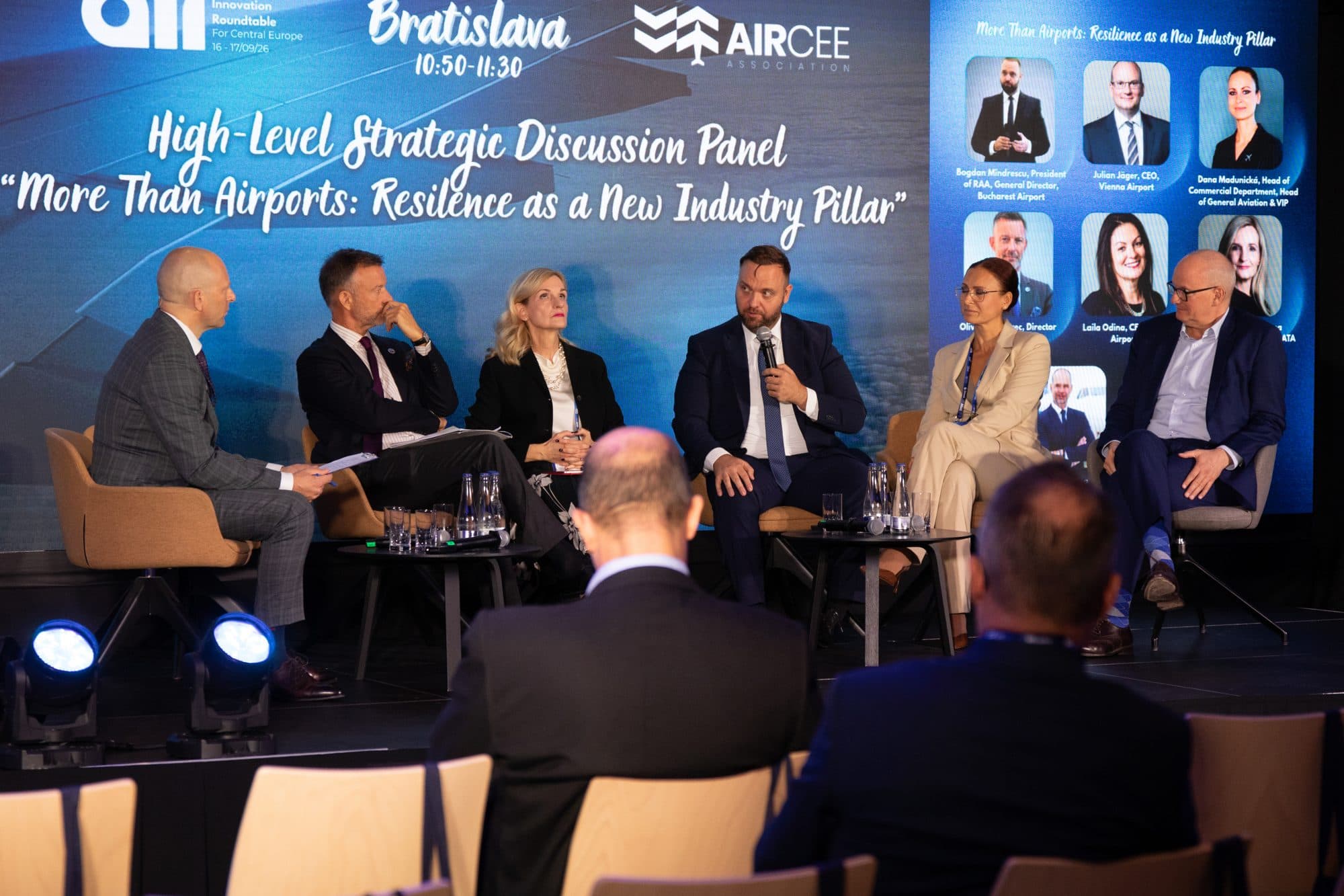 Six panellists and a moderator on stage in front of a board naming the participants.